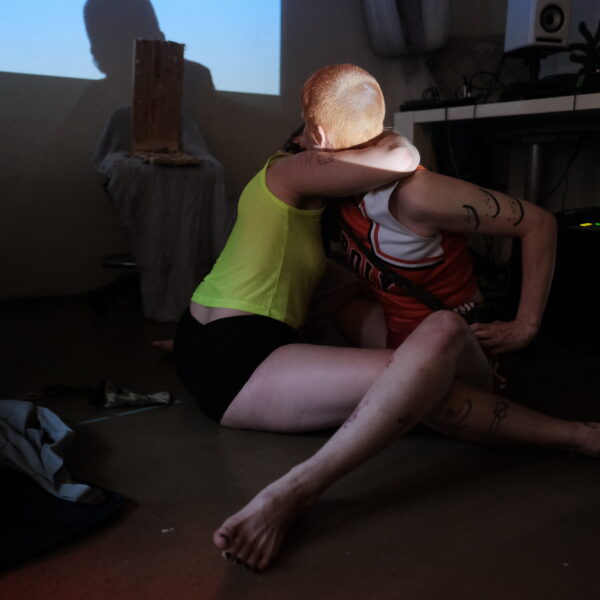 two bodies entangled, in a dark room with the light of a big screen in the background.